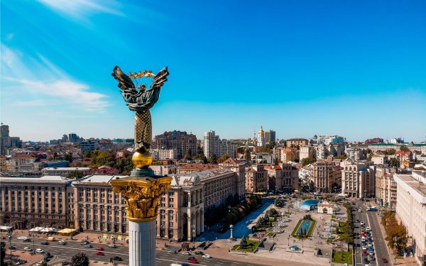 Oversiktsbilde over sentrum og et torg i Kyiv i Ukraina, med blå himmel og en statue.